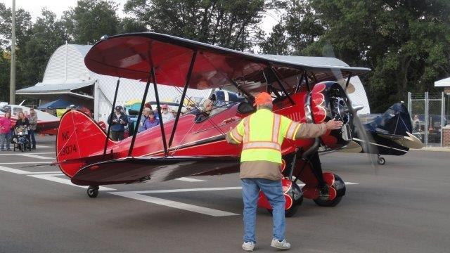 A red Biplane is readying for take off and is being guided by a crew member